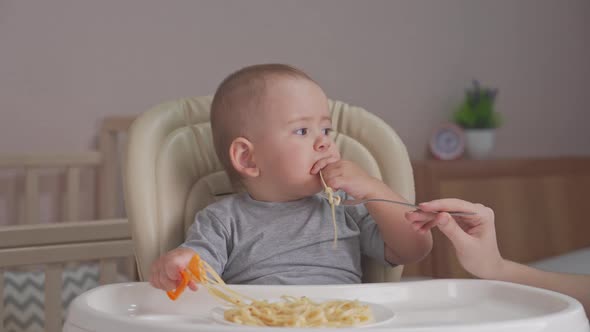 Mom feeds a newborn baby aged 12-17 months spaghetti with tomato sauce.