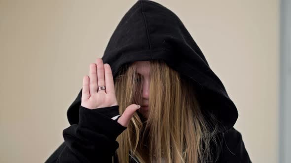 Teenage Girl Covering Her Face with a Hood Demonstrates a Gesture Indicating a Person's Need for