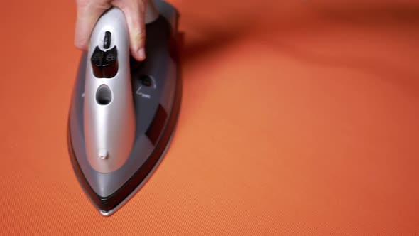 Female Hand Ironing a Bright Orange Cloth with a Steam Iron on an Ironing Board