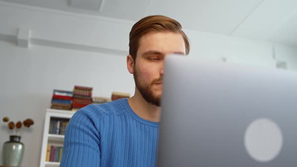 Smiling young man using laptop, studying online, working from home, typing on laptop