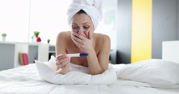 Frightened Woman Looking at Pregnancy Test While Lying on Bed