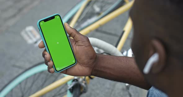 Close Up of African American Man in Earphones Holding His Smartphone Looking To Green Screen. He