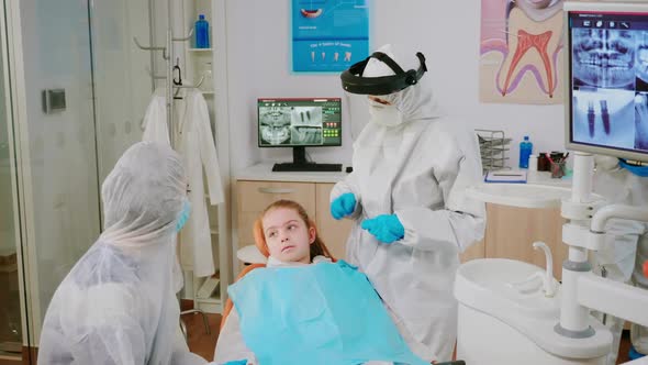 Pediatric Dentist in Protective Shield Checking Teeth of Little Girl