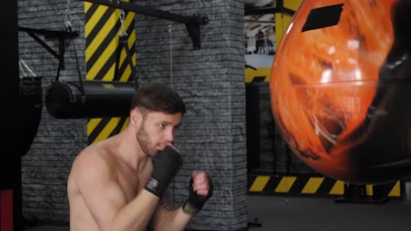 Handsome Young Boxer is Exercising with a Punching Bag at the Gym