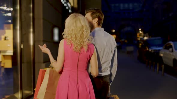 Beautiful Couple Strolling Through Evening Market Street Looking at Shop Windows