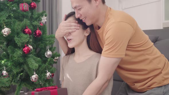 Asian couple man giving christmas gifts to his girlfriend in their living room at home.