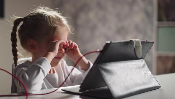 Tired Girl Rubs Eyes Stretching at Video Lesson Via Tablet