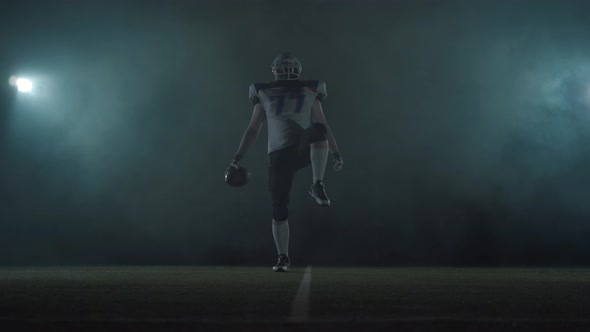 American Football Sportsman Player in Football Helmet Standing on the Field on Black Background in a