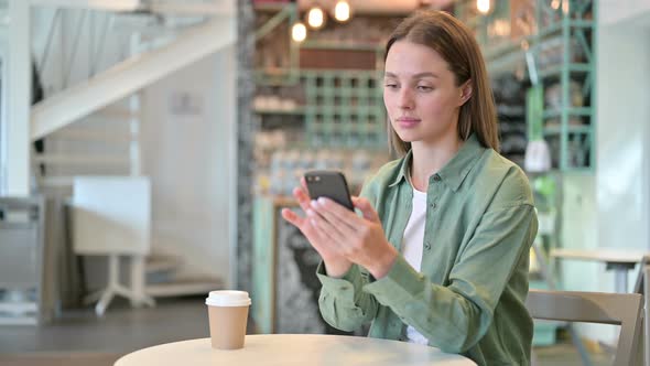 Serious Young Woman Using Smartphone in Cafe 