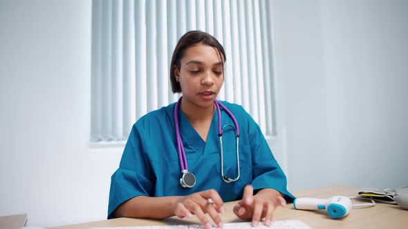 Female Doctor Sits at Workplace Looks at the Camera and Communicates with the Patient Via Video Call