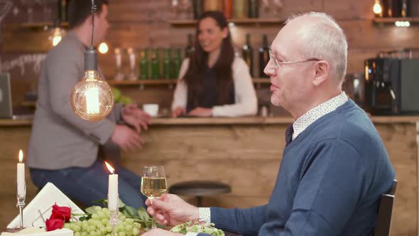 Cheerful Old Man on a Date Clinking a Glass of White Wine