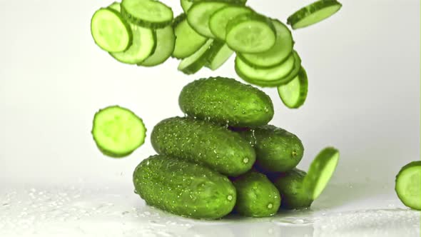 Super Slow Motion Pieces of Cucumber Fall on a Bunch of Cucumbers on the Table