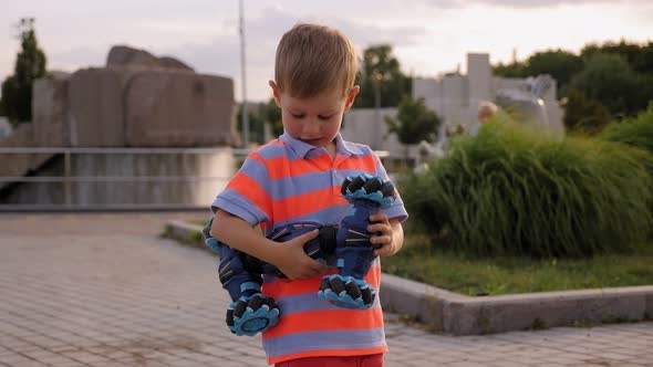 A Little Boy Holds a Modern Robot Car on the Remote Control in a Park