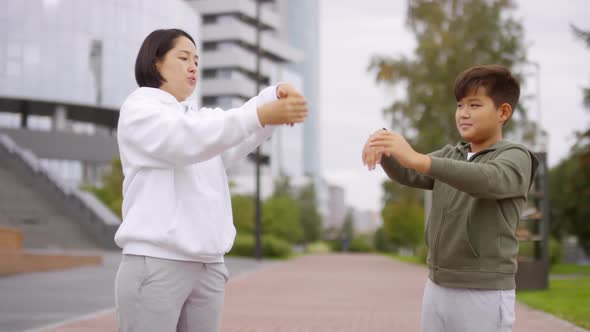 Asian Woman and Boy Stretching Wrists during Outdoor Workout