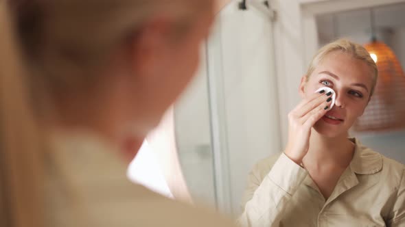 Positive blond woman wiping her face with a sponge at mirror