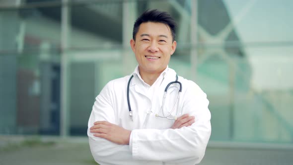 Close up portrait of Asian doctor looking at camera with arms crossed on background 
