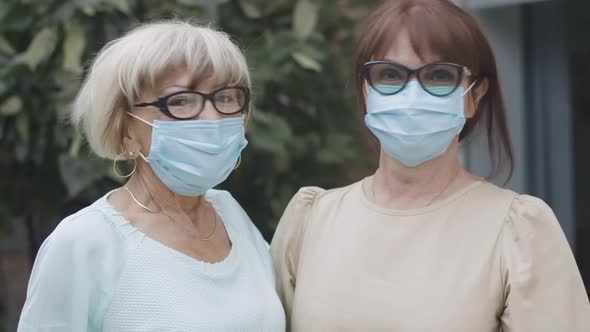 Closeup of Cheerful Senior Caucasian Women in Eyeglasses and Coronavirus Face Masks Looking at