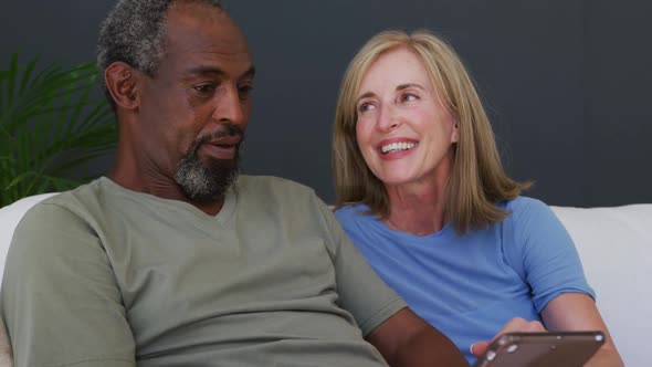 Mixed race senior couple using digital tablet while sitting on the couch at home