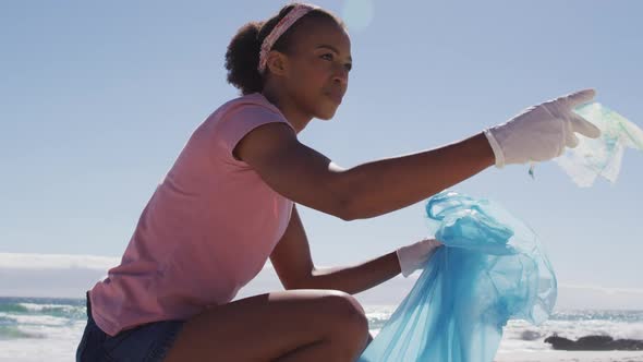 African american woman collecting plastic waste on the beach