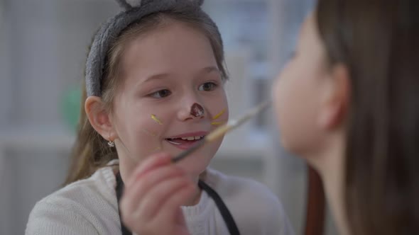 Joyful Little Girl Painting Sister Face with Food Coloring Smiling Enjoying Easter Fun