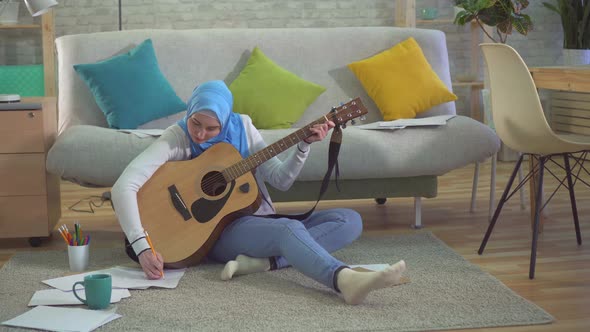 Young Muslim Woman in a Hijab Sitting on the Floor Playing Guitar and Recording Chords