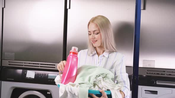 Portrait of an Attractive Blonde in a Public Laundry Room Next To a Washing Machine and Holding a