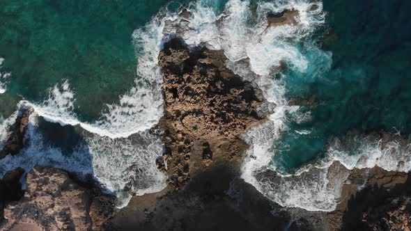 Top-down lowering over ocean waves crashing on rocky coast near Porto dos Frades, Madeira