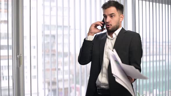 A young company manager speaks angrily on the phone, shakes documents and drops