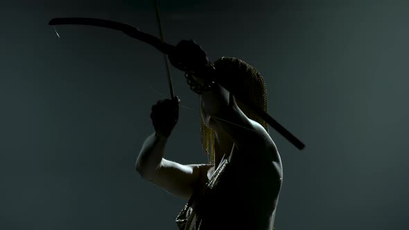 Silhouette of Dancing Joan of Arc with Bow and Arrow on Stage in a Dark Studio with Smoke and Neon