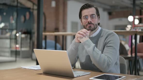 Young Man Thinking While Working on Laptop in Office