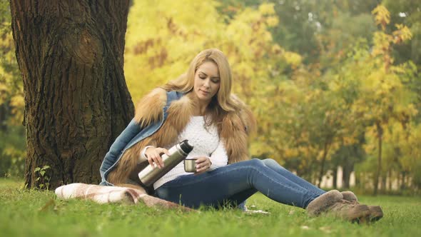 Woman Pouring Hot Tea From Thermos, Warming Beverage, Picnic in Autumn Forest
