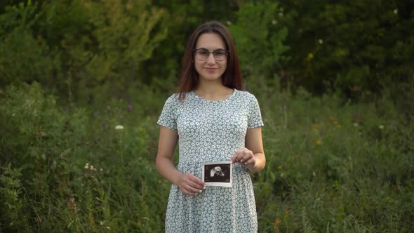 A Young Pregnant Woman Holds an Ultrasound Picture of a Baby in Her Hands