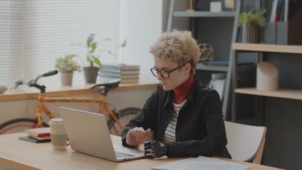 Young Woman with Prosthetic Arm Using Laptop in Office