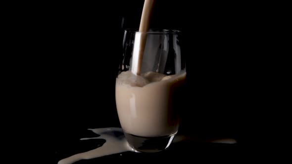 Vegan hazelnut milk being poured in glass, spills over onto black surface table. Slow motion.