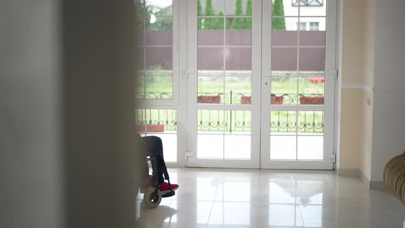 Wide Shot Glass Door in Living Room with Teenage Girl Rolling Wheelchair with Disabled African