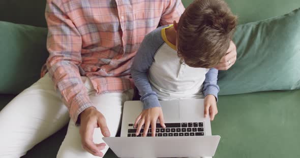 Father and son using laptop on sofa at home 4k