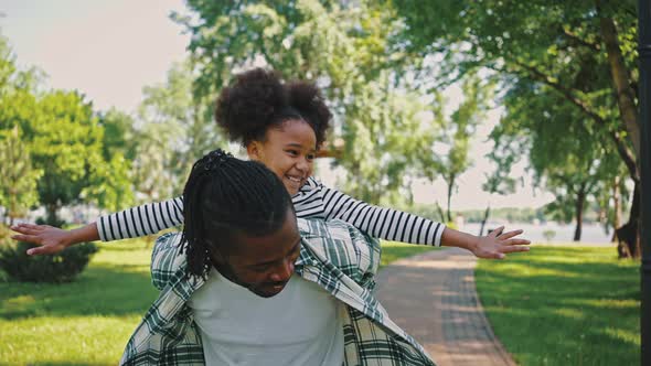 Excited African Ethnicity Girl Has Fun Sitting on Her Fathers Back