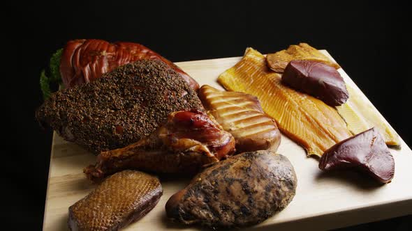 Rotating shot of a variety of delicious, premium smoked meats on a wooden cutting board