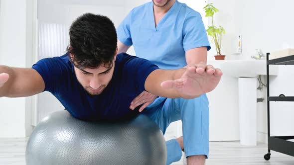 Physiotherapist Helps Handsome Young Patient for Doing Pilates Exercises with Ball