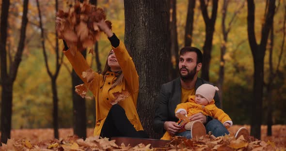 Happy Young Family with Little Baby at the Autumn Park Mom Throws Up a Leaves