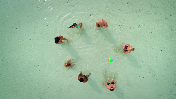 Aerial view of group of friends in swimwear playing volleyball in sea near beach.