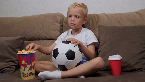 Little Boy Is Watching a Football Match on TV Sitting on the Couch with Popcorn.