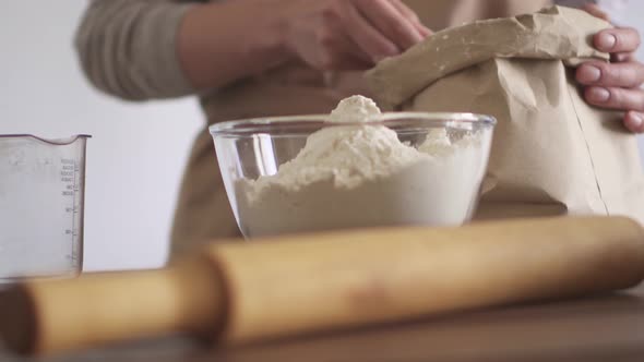 Chef girl puts flour with wooden spoon from paper bag in glass bowl. Measuring glass measuring spoon