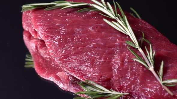 Raw organic beef meat with rosemary spinning on dark background