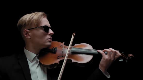 Young Caucasian Male in Black Suit and Glasses Plays Violin on Dark Background