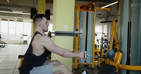 Young Muscular Athlete Works Out in a Modern Gym on Seated Row Machine