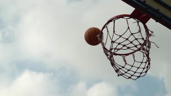 Thrown Orange Basketball Hits the Basket on an Outdoor Court in the Shade of Trees