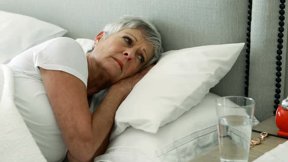 Senior woman turning off alarm clock in bedroom
