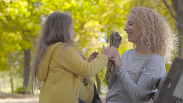 Two Little Cute Caucasian Sisters Giving Their Mom Flowers and Kissing Her