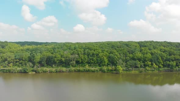 drone right flight of black cars driving through an Illinois forest on a country road next to a lake